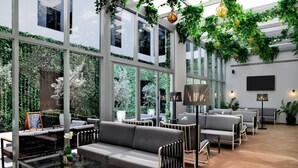 A modern indoor seating area with glass walls, green plants, and contemporary furniture. - The District Hotel (Dubai)