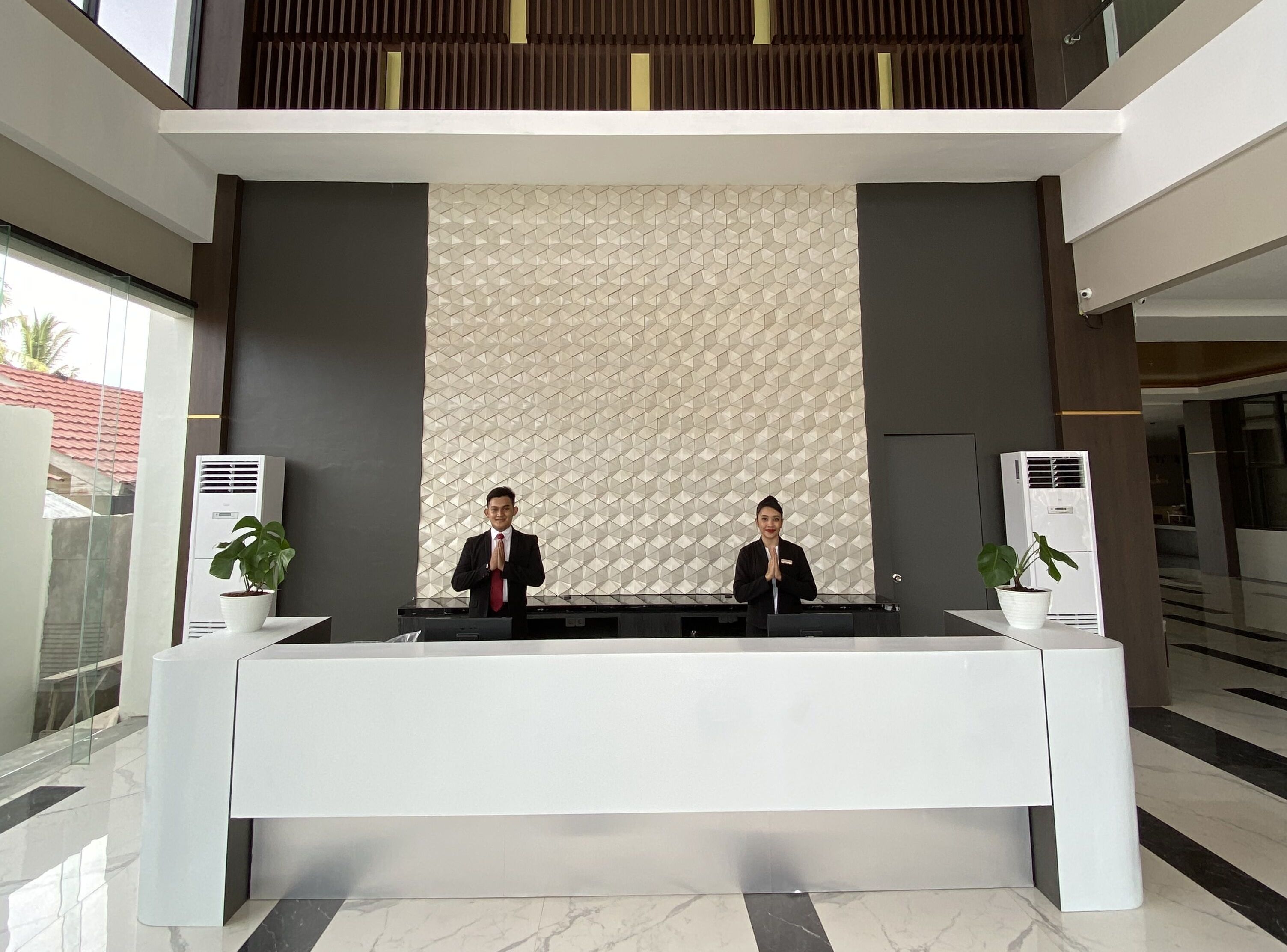 A reception desk with two staff members, air conditioning units, and potted plants.