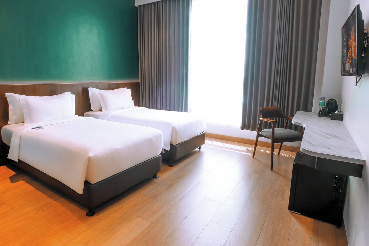 Habitación de hotel con dos camas, un escritorio, una silla y un televisor.