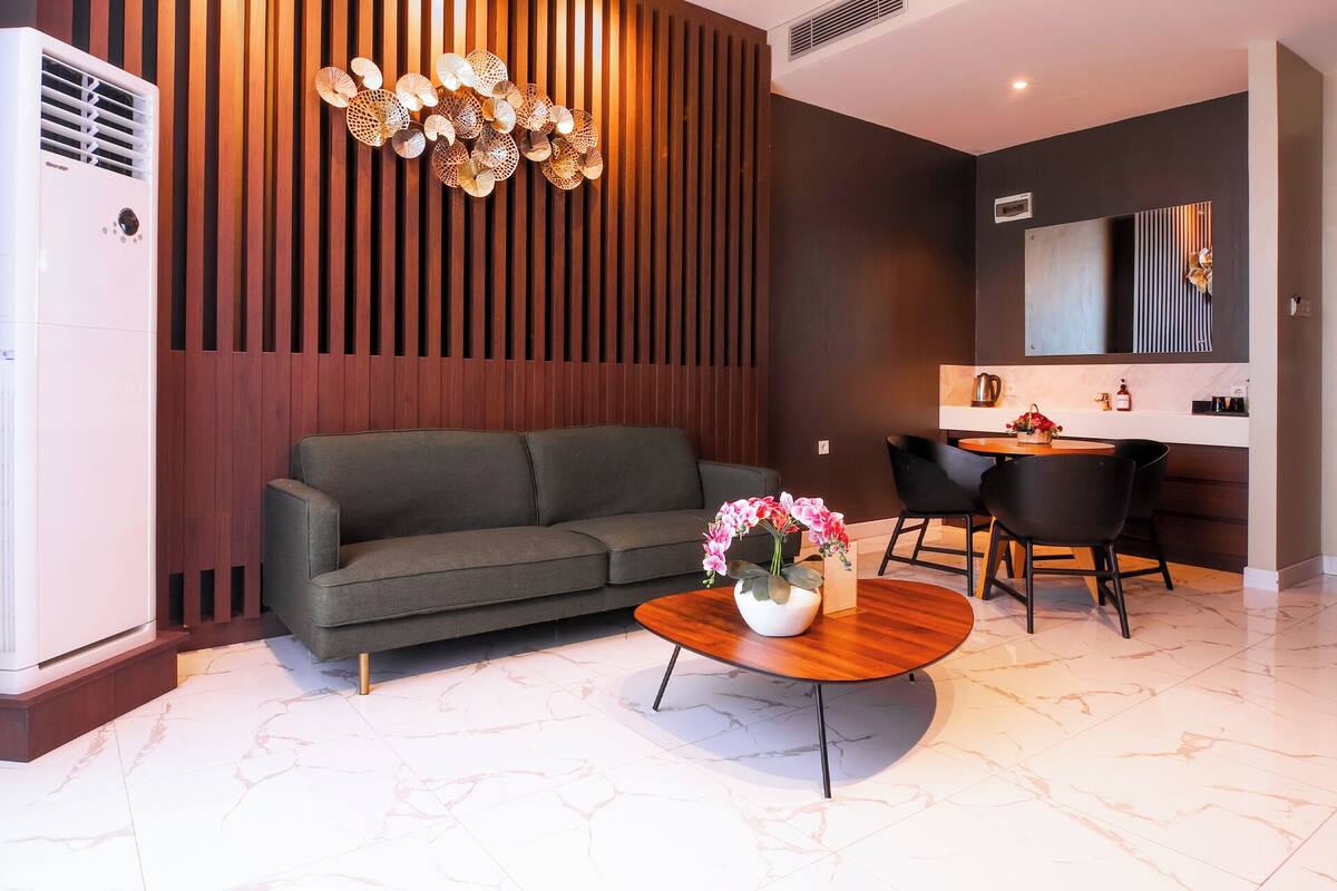 Una sala moderna con sofá, una mesa redonda con flores, un comedor con mesa y sillas, y una zona de cocina con estufa y microondas.
