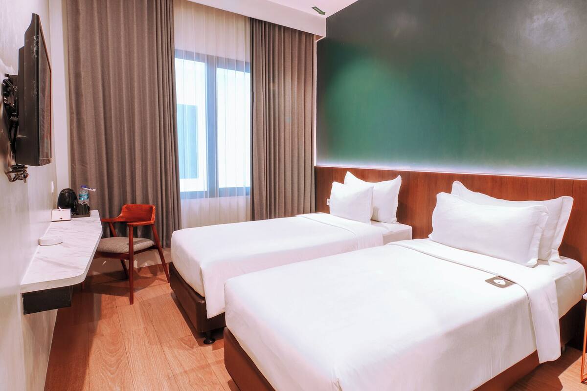 Habitación de hotel con dos camas, un escritorio, una silla, un televisor y una pared verde grande.