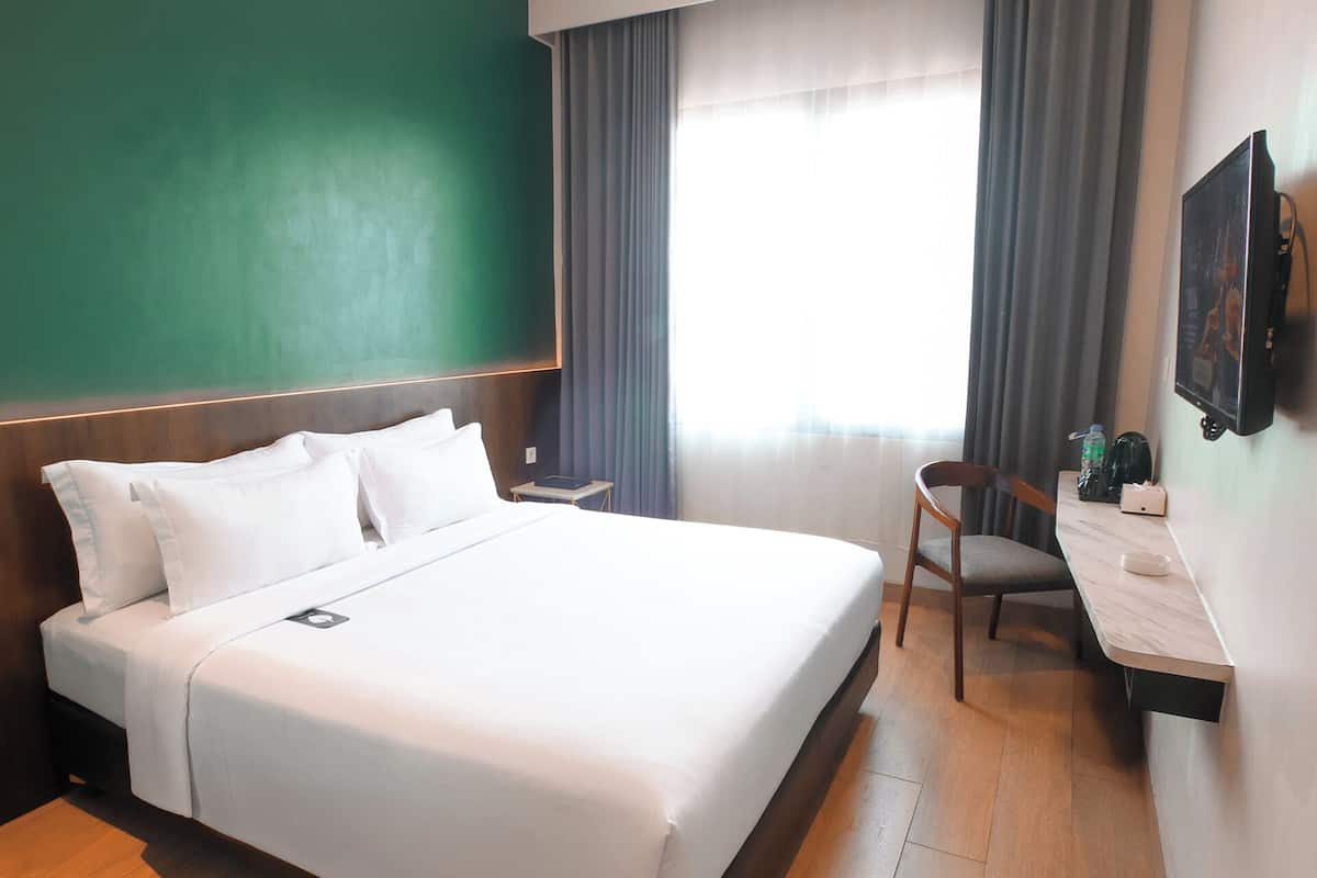 Habitación de hotel con cama, escritorio, silla, televisor y ventana con cortinas.