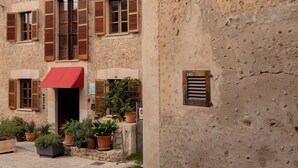 A building with multiple windows, some with shutters, and a red awning. There are potted plants in front of the building. - Marton Turisme de Interior (Valldemossa)