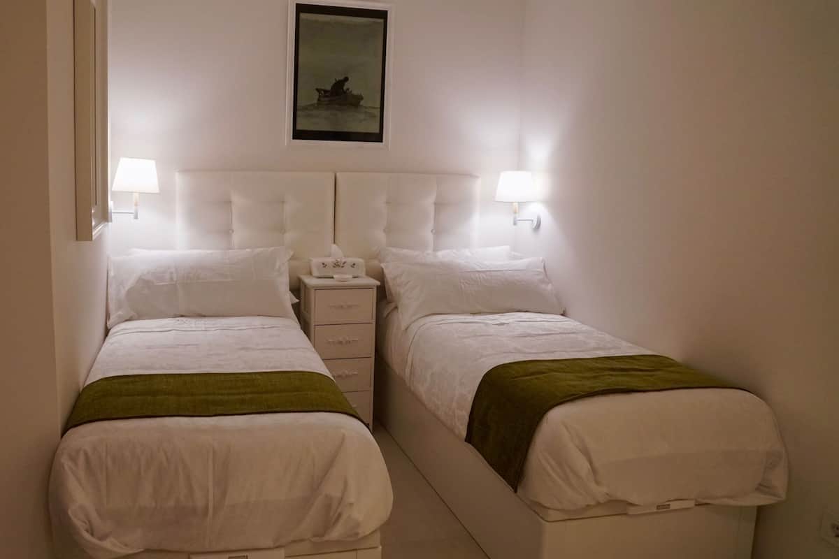 A double bed with a green throw, a nightstand with a lamp, and a framed picture on the wall.