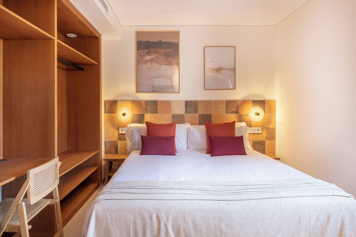 A hotel room with a bed, bedside tables, a desk, and a wardrobe.