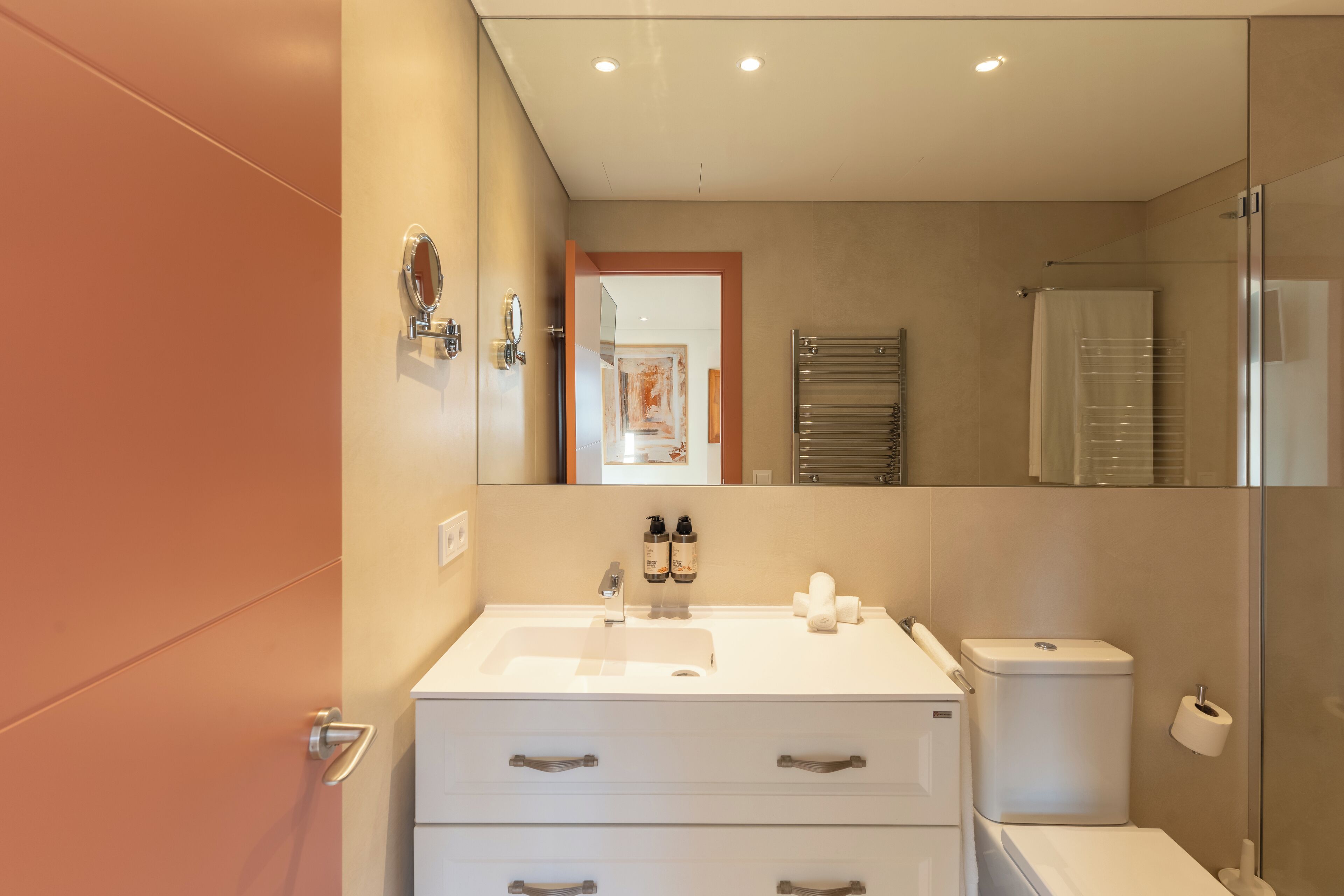 A modern bathroom with a white sink, two drawers, a toilet, and a glass shower enclosure.