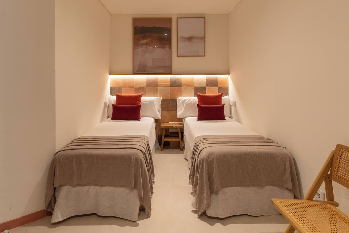 A hotel room with two beds, a small table, and a chair.