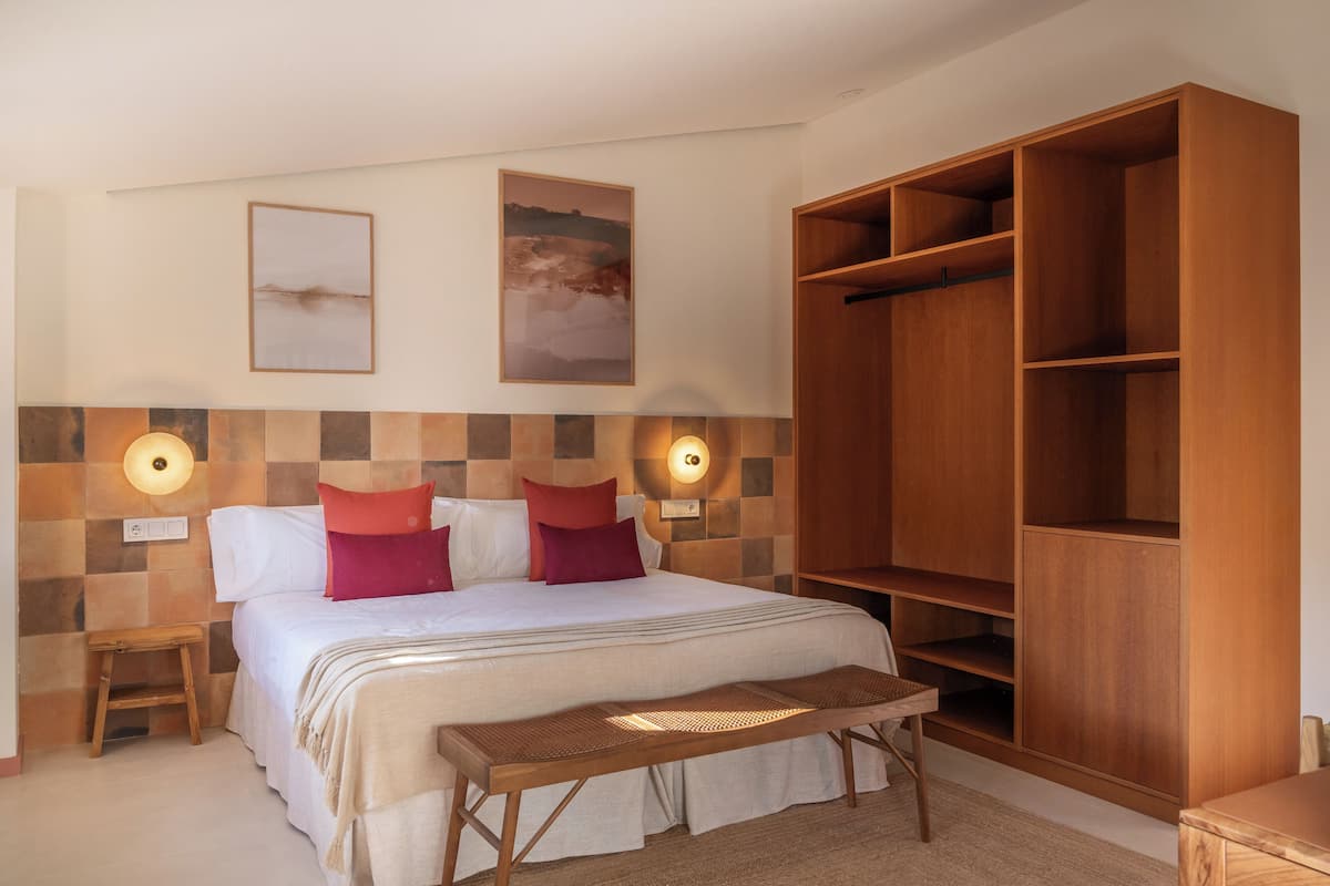 A hotel room with a bed, wooden wardrobe, and two wall-mounted lights.