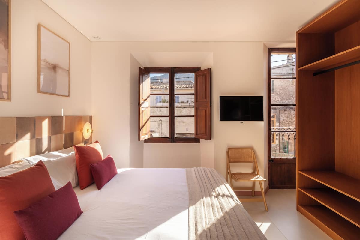 A bedroom with a bed, pillows, a chair, a TV, and a window with a view of buildings.