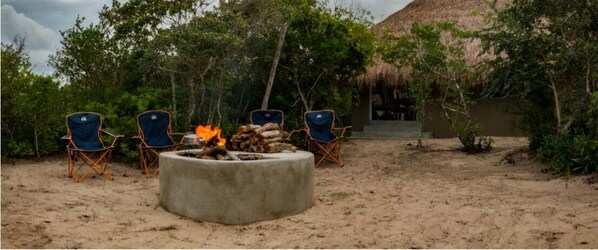 A sandy outdoor area with a concrete fire pit surrounded by four blue folding chairs.