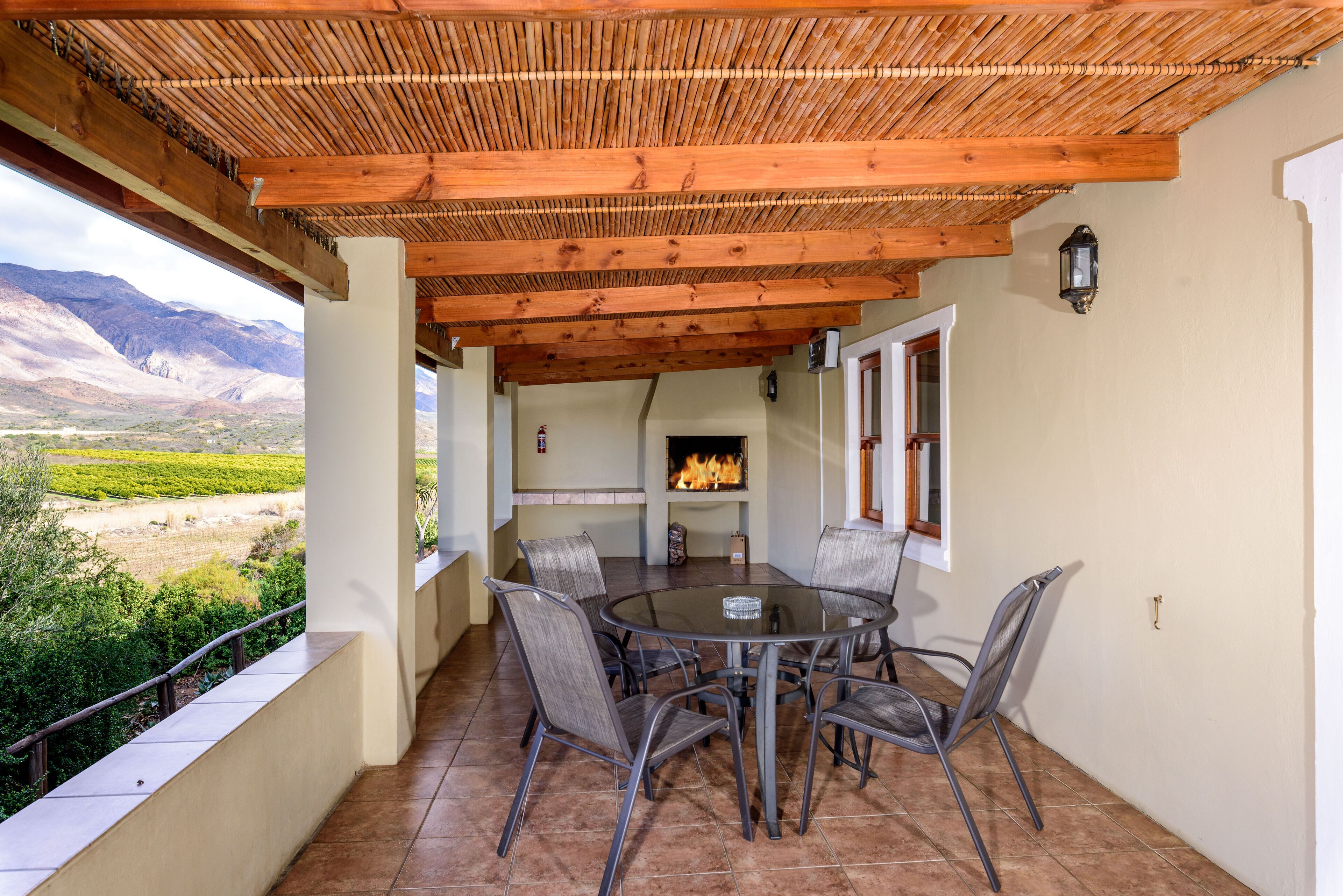A covered patio with a round table and chairs, a fire pit, and a view of a mountainous landscape.