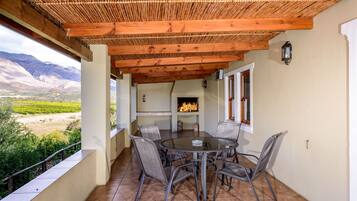 A covered patio with a round table and chairs, a fire pit, and a view of a mountainous landscape.