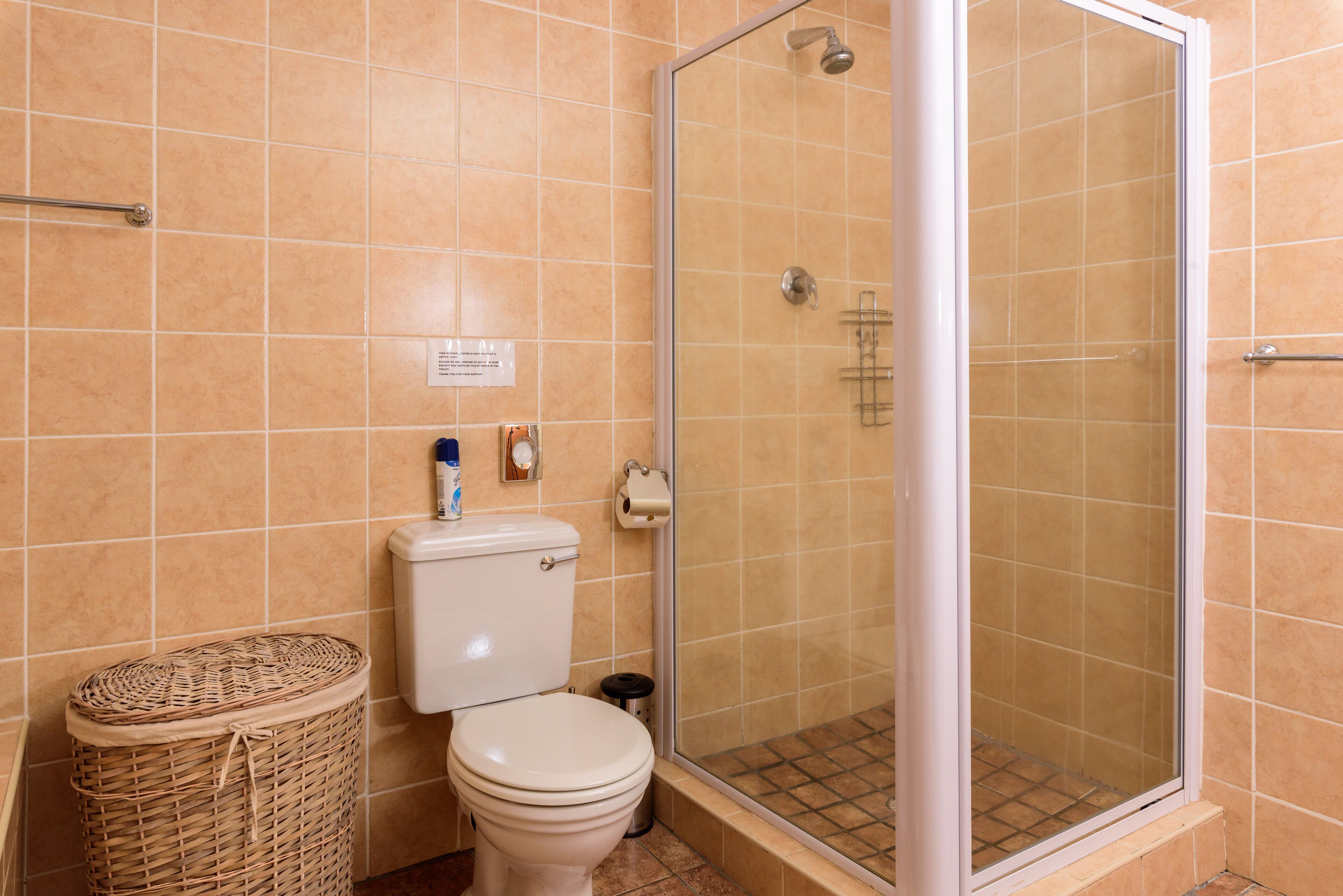 Un baño con inodoro, una cesta de mimbre y una ducha con paredes de vidrio.