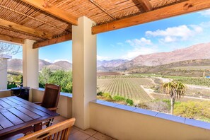 Un espace extérieur abrité, doté d’une table et de chaises, qui offre une vue sur un paysage montagneux avec des champs.