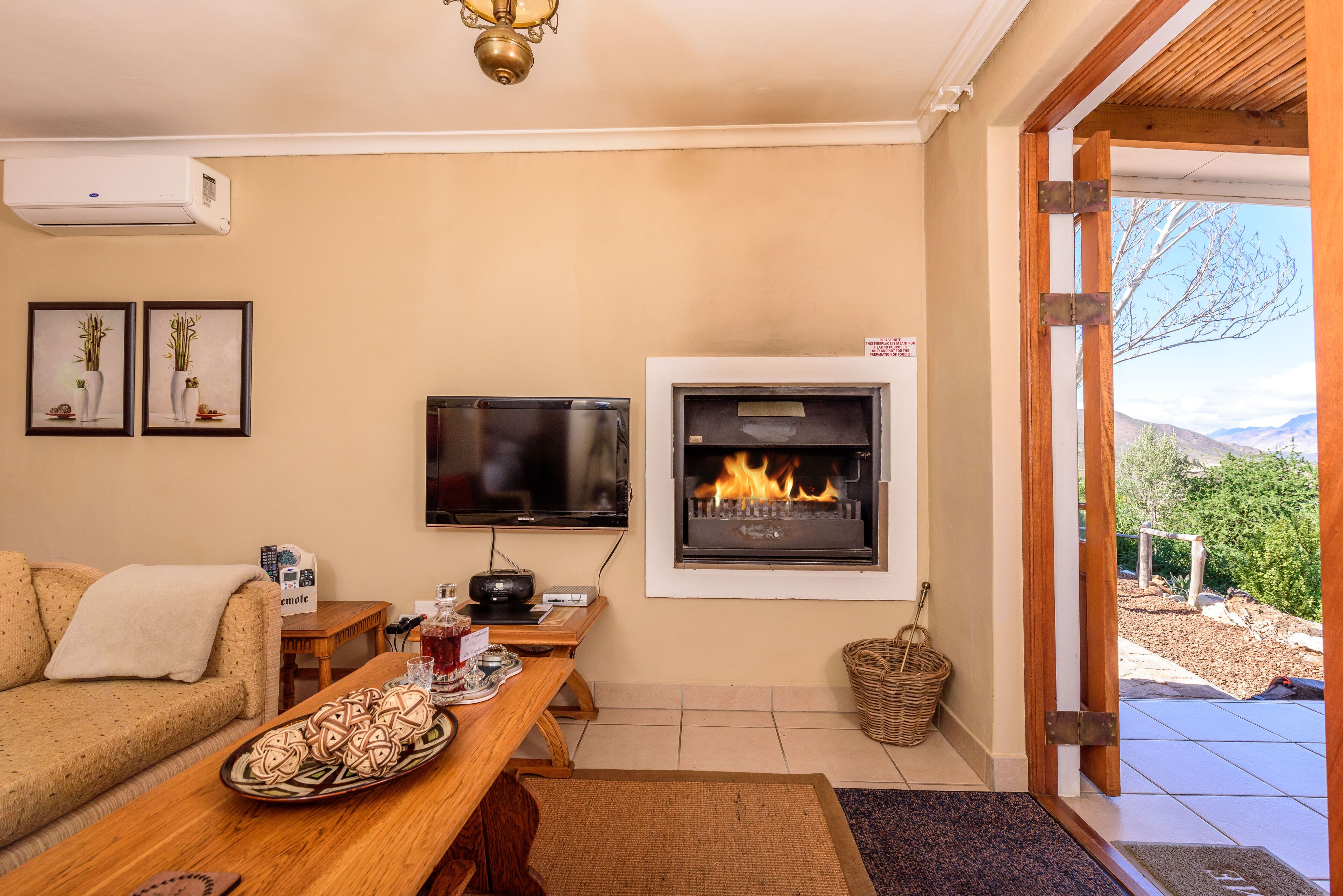 Una sala de estar con chimenea, un sofá, una mesa de centro con aperitivos, un televisor y vistas al exterior.