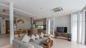 A modern living room with a grey sofa, a wooden coffee table, and a TV stand. - 3 Bedroom Civetta Pool Villa (Rawai)