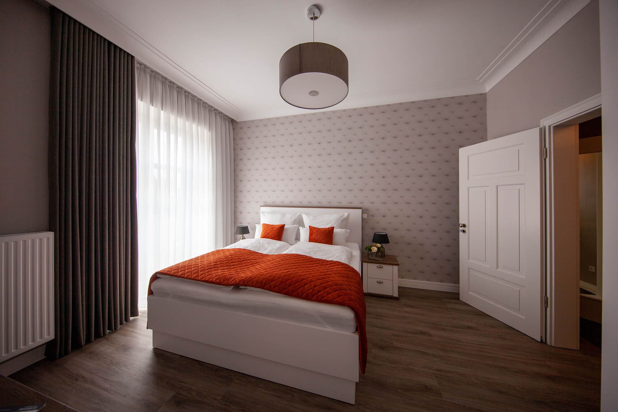 Een slaapkamer met een bed, nachtkastje, deur en raam met gordijnen.