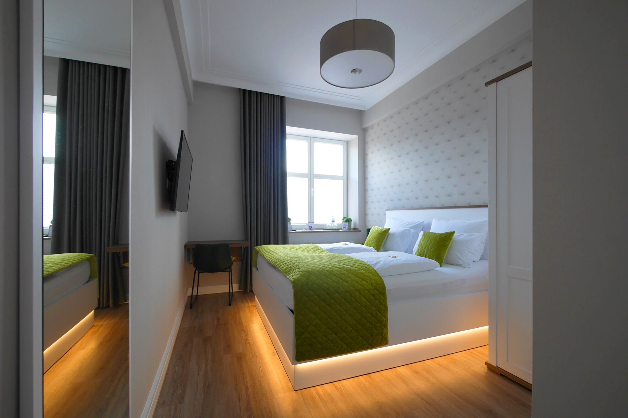 Habitación de hotel moderna con cama, escritorio, silla, televisión y ventana con cortinas.