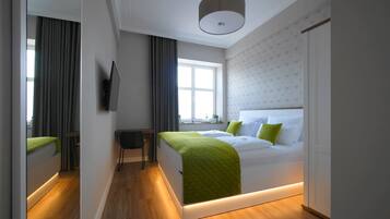 Habitación de hotel moderna con cama, escritorio, silla, televisión y ventana con cortinas.