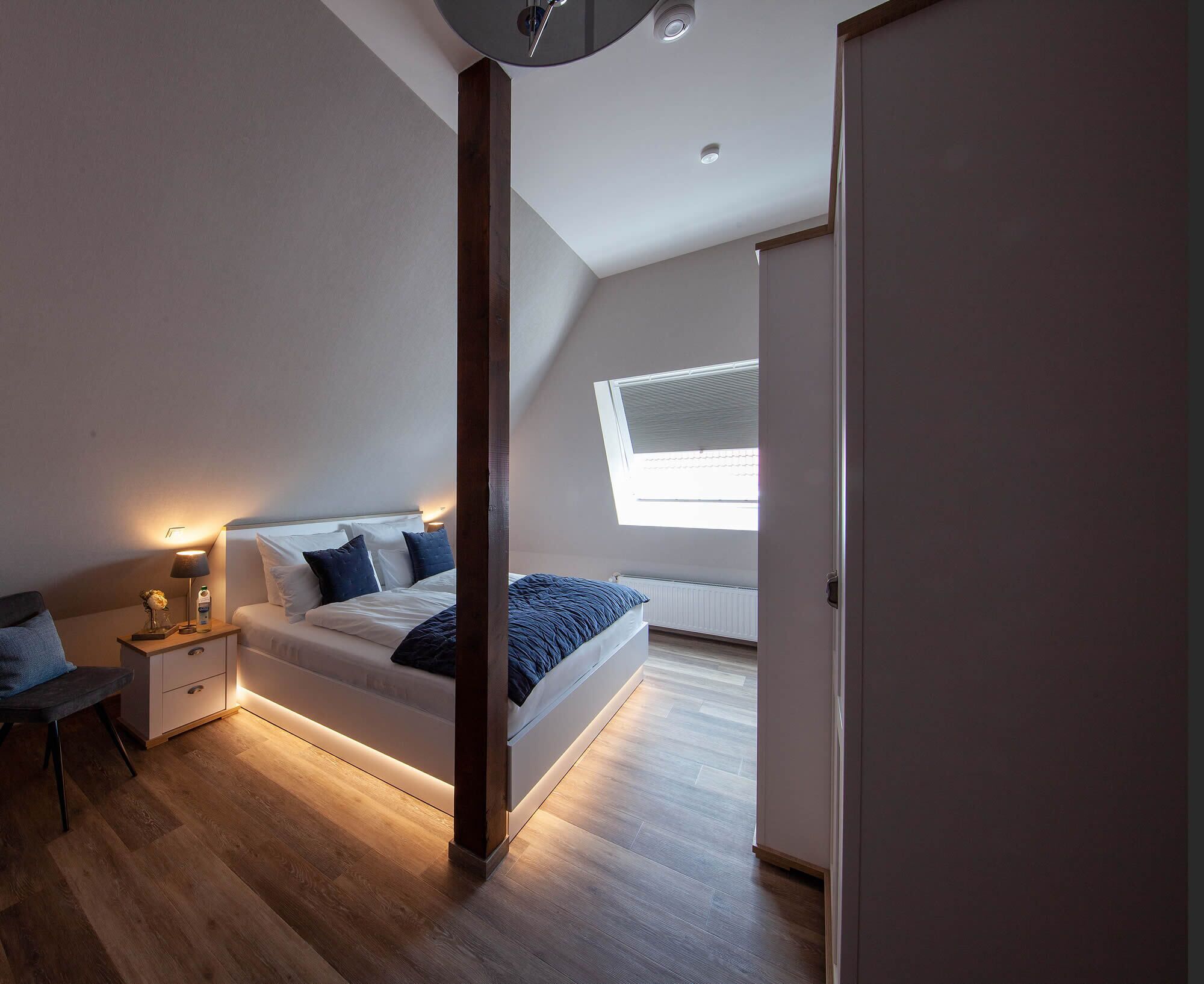 Une chambre à coucher moderne, avec un lit, une table de chevet, une lampe et une vue sur l’extérieur par une fenêtre.