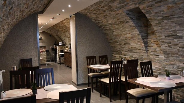 En restaurang med väggar av sten och ett högt tak, inredd med bord och stolar som är placerade för att skapa en trevlig matplats.
