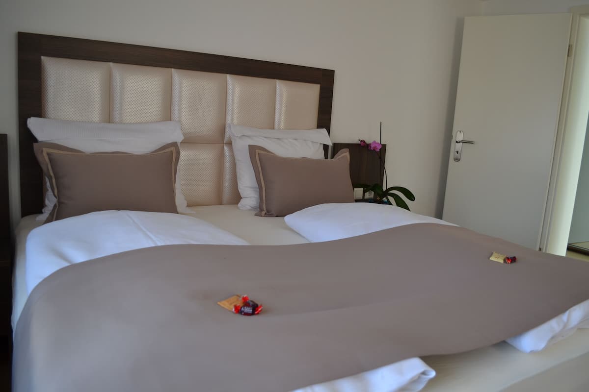 Cama doble con cabecera, dos almohadas y mesita de noche con lámpara.