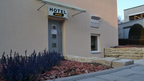 Ett hotell som heter ”MYRSINI”, med en skylt ovanför dörren, ett litet fönster och en stenmur med växter framför.