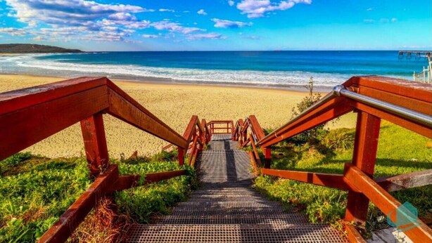 Uma escadaria de madeira leva a uma praia com vista clara para o oceano.