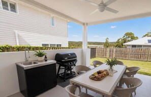 Un área de cocina al aire libre con una parrilla, un lavamanos y una mesa de comedor con sillas.