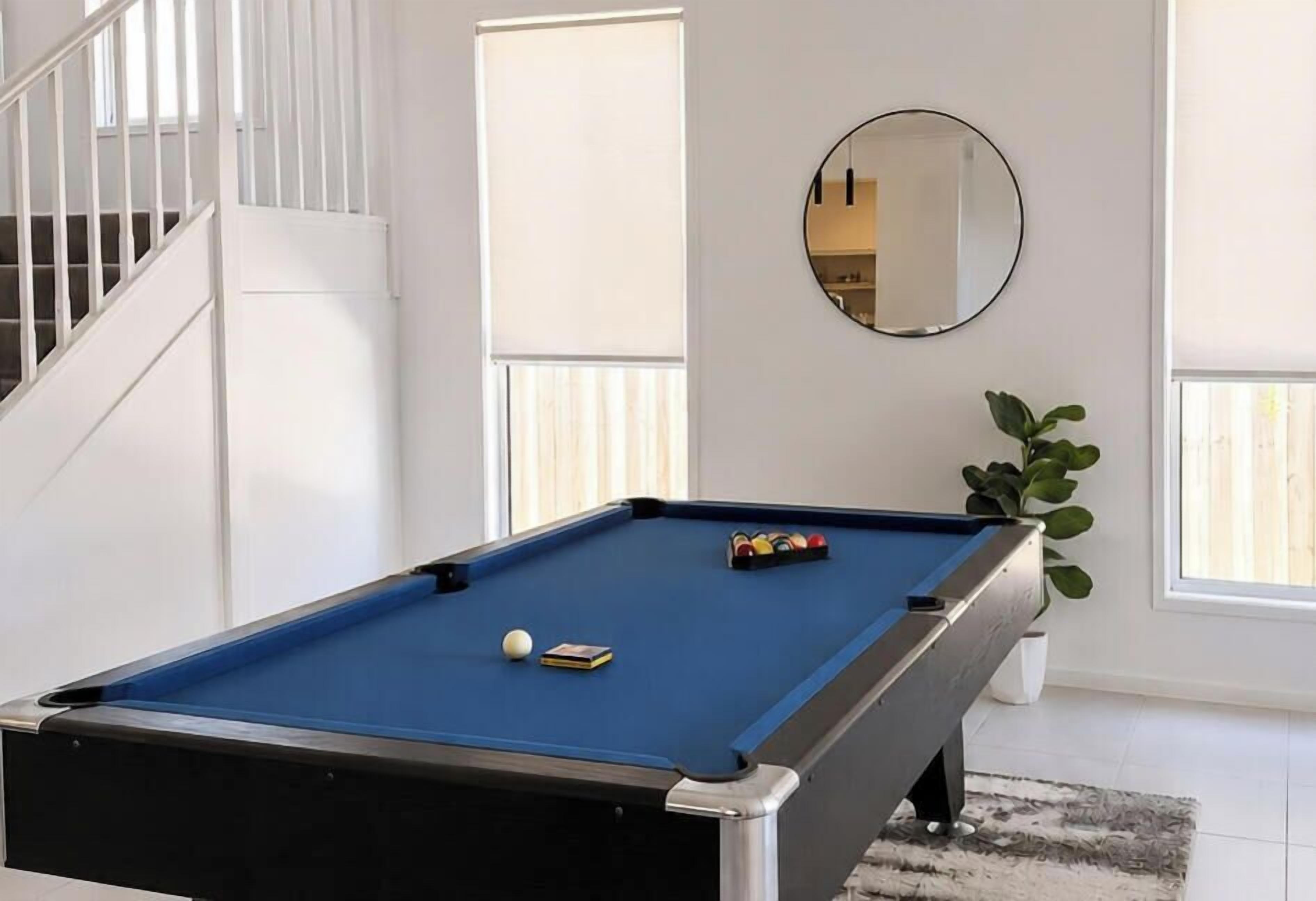 Une table de billard dans une pièce avec un escalier et une plante en pot.