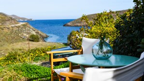 Mesa com um vaso de vidro e uma cadeira, com vista para a paisagem costeira, colinas e o mar.