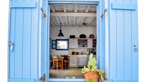 Uma porta azul dá acesso a uma cozinha com armários brancos, uma mesa de jantar e um cacto.