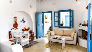 Uma sala de estar com um sofá branco, uma cadeira de vime, uma mesa de centro e uma lareira.