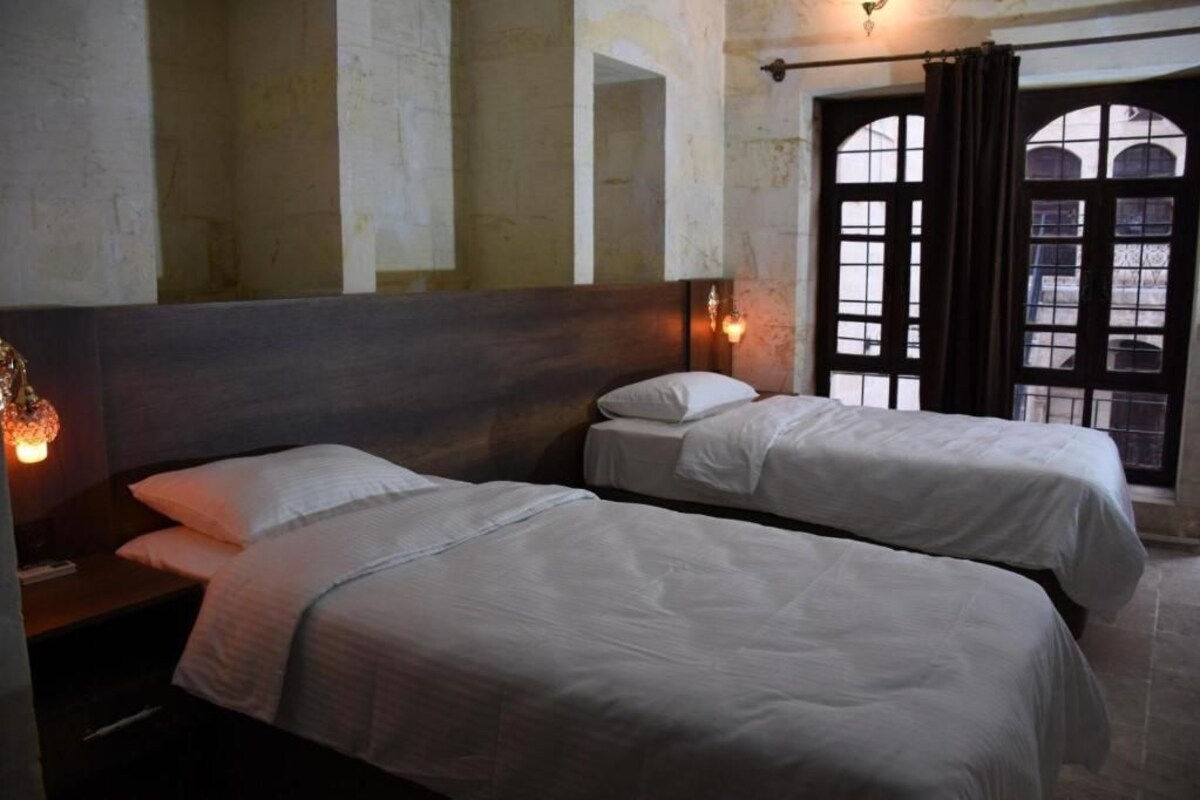 Quarto com duas camas, cabeceira de madeira e janela com cortinas.