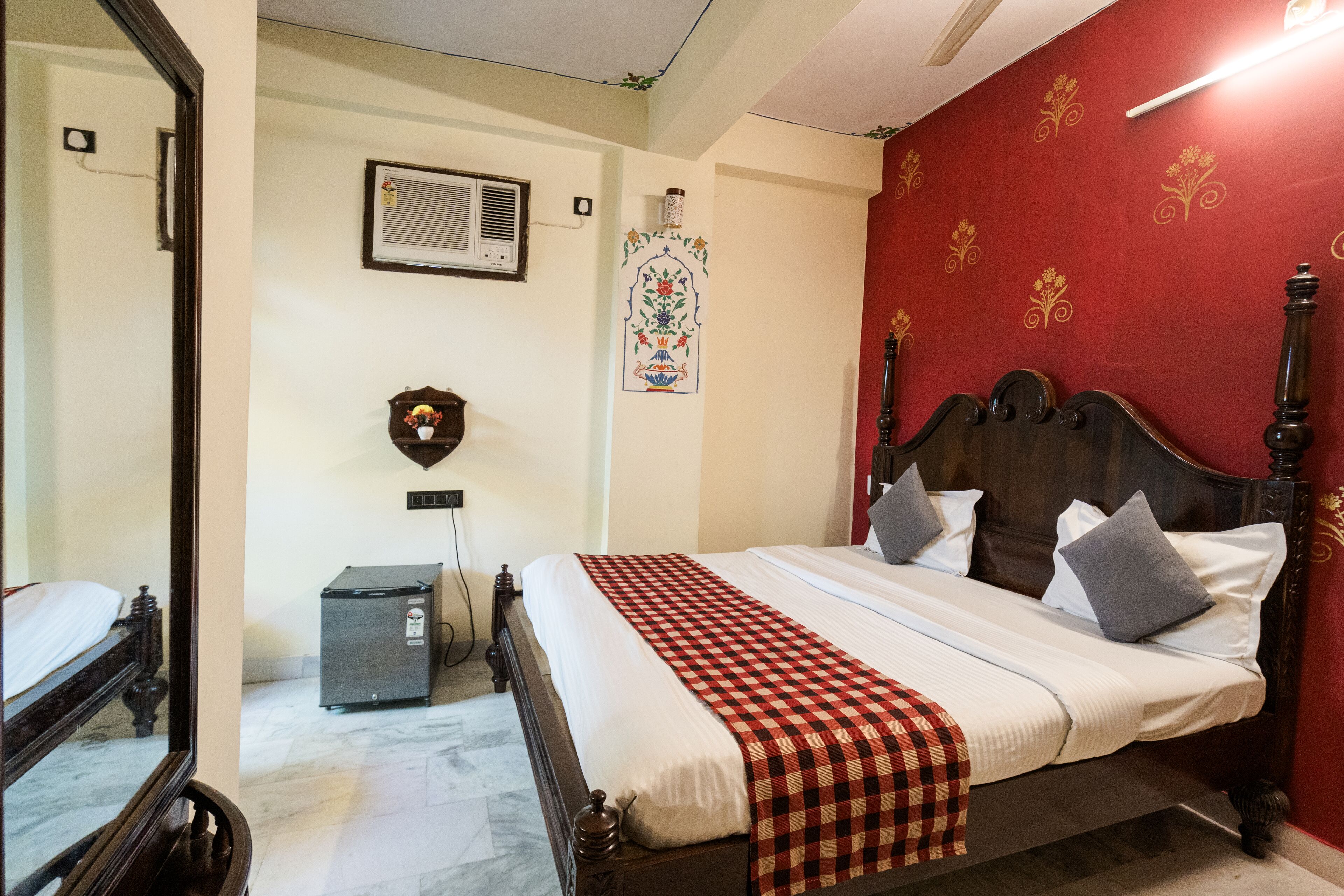 A bedroom with a wooden bed, a red accent wall, a small heater, and a mirror.