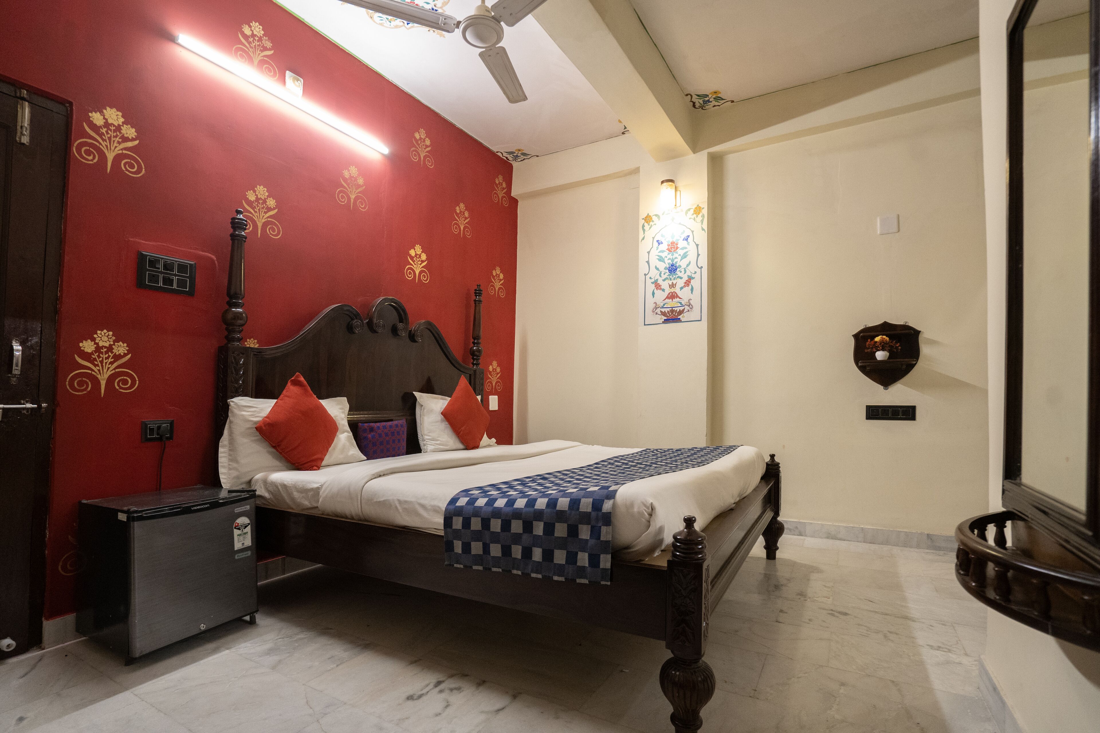 A bedroom with a bed, a nightstand, a heater, a wall-mounted clock, and a decorative mirror.