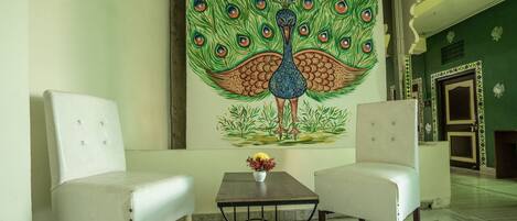 Una habitación con dos sillones blancos, una mesita con un jarrón de flores y un amplio mural de un pavo real en la pared.