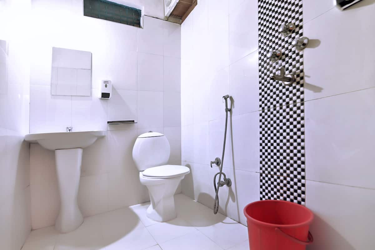 A bathroom with a white sink, toilet, and shower. There is a red bucket on the floor.