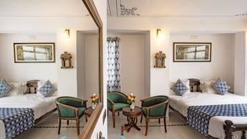 A hotel room with two beds, green upholstered chairs, a small table with a vase of flowers, and framed pictures on the walls.