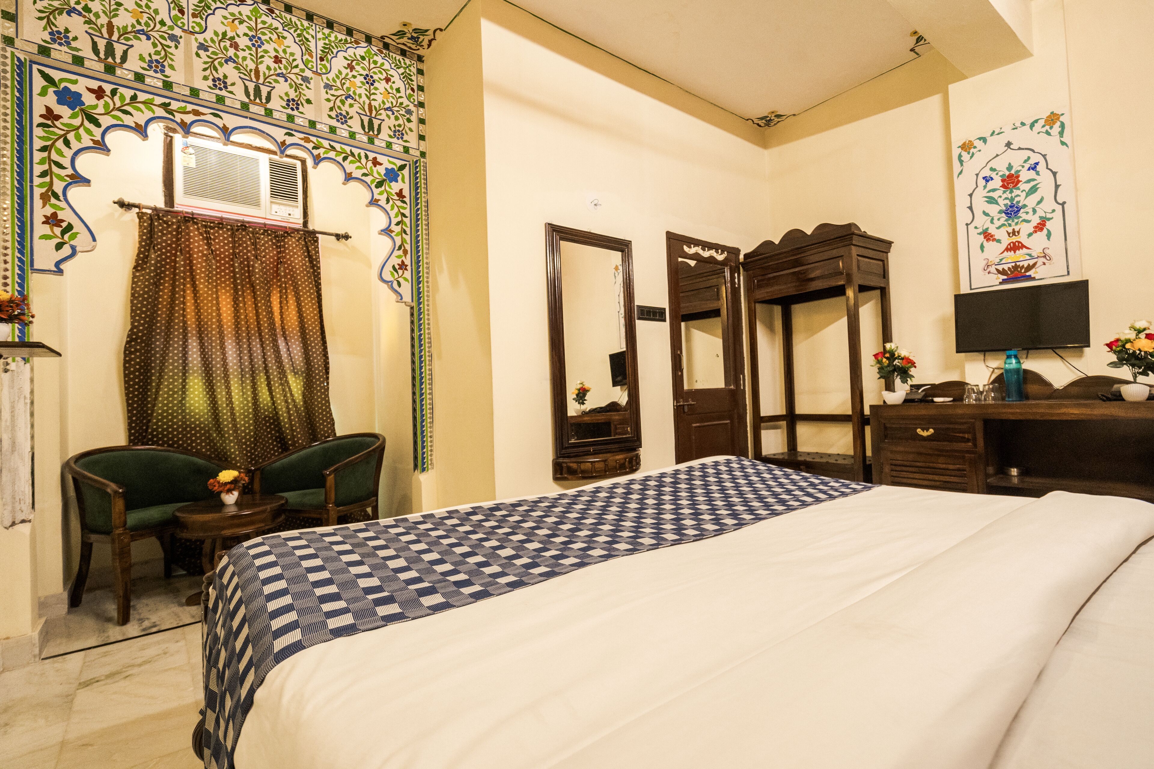 Une chambre d’hôtel avec un grand lit, deux chaises, une petite table, un miroir, une commode et un téléviseur.