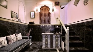 A lobby with a marble floor, a sofa with floral cushions, a reception desk, and a staircase. - The Lake View Hotel – On Lake Pichola (Udaipur)