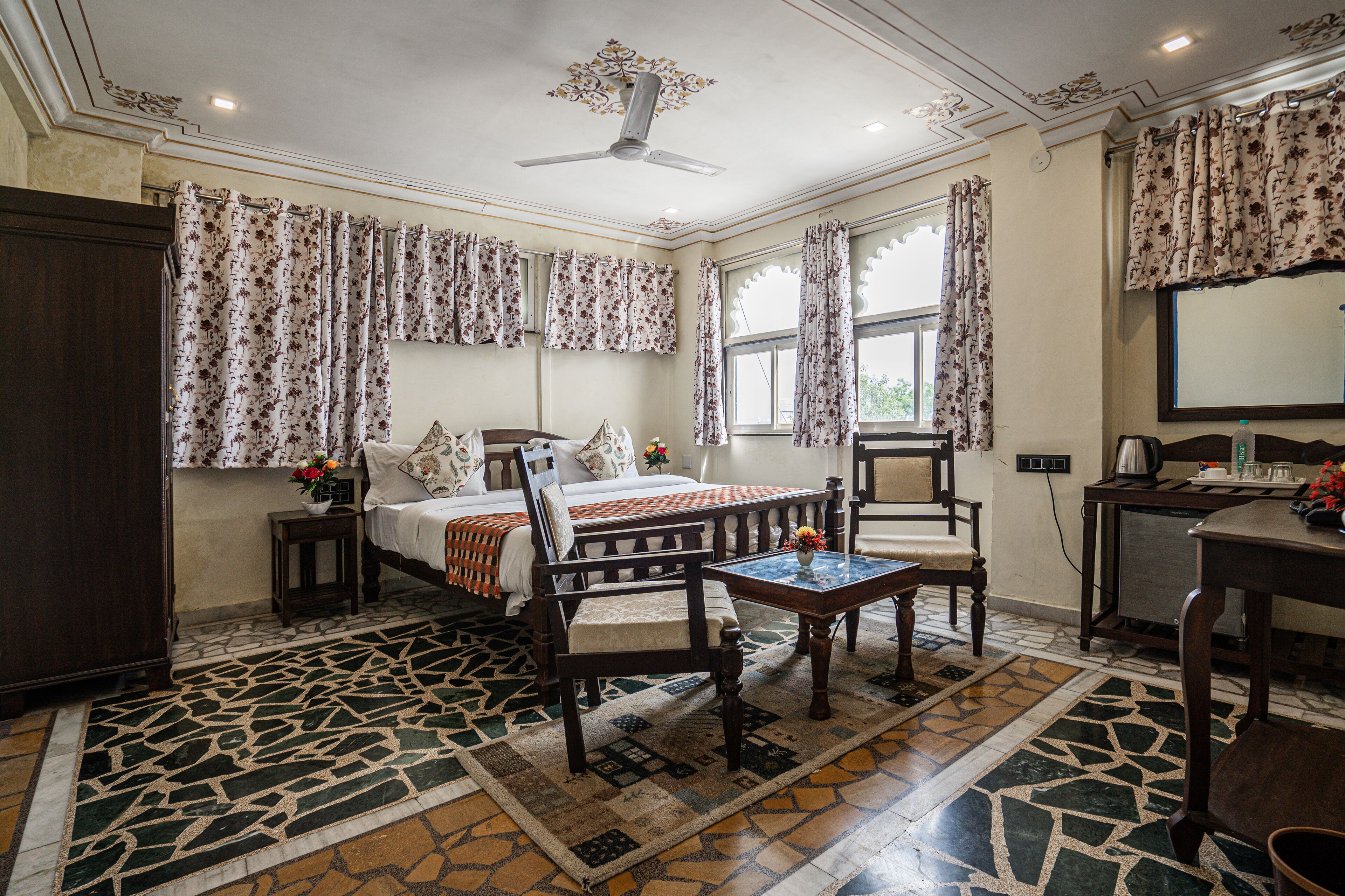 Una habitación con cama, dos sillas, una mesa, un escritorio y un ventilador de techo.