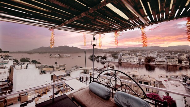 A balcony with a view of a river and cityscape at sunset. - The Lake View Hotel – On Lake Pichola (Udaipur)
