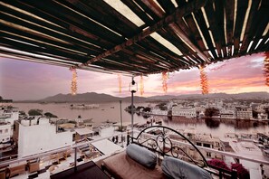 A balcony with a view of a river and cityscape at sunset. - The Lake View Hotel – On Lake Pichola (Udaipur)
