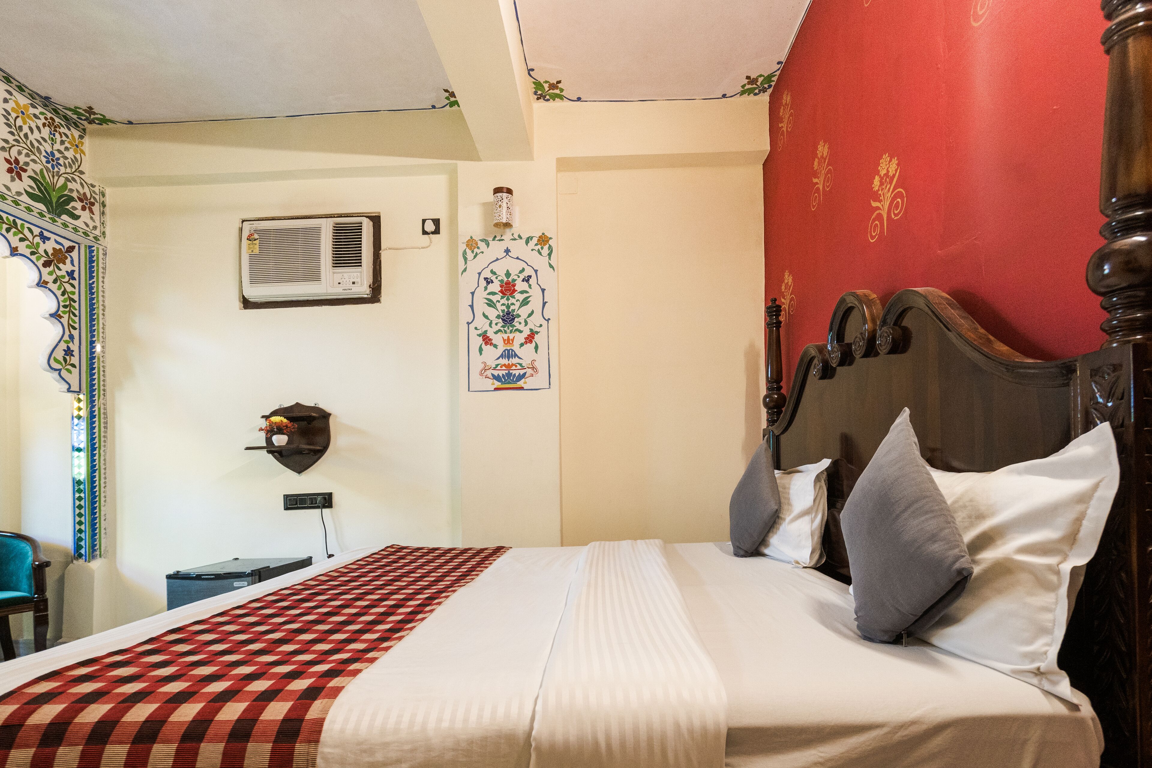 A neatly made bed with a checkered bedspread, a wooden headboard, and a wall-mounted air conditioner.