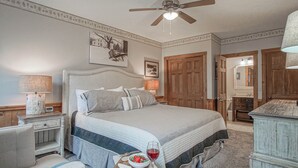Een slaapkamer met een groot bed, een plafondventilator, een nachtkastje met een lamp en een dressoir.