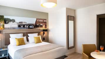 A hotel room with a large bed, a bedside table, a chair, a small table with a bowl of fruit and a glass of orange juice, and a large mirror.