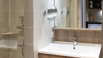 Une salle de bain moderne avec une douche en verre, un lavabo blanc, des meubles en bois et un grand miroir.