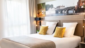 A hotel room with a large bed, a headboard with a cityscape mural, a bedside table, and a window with sheer curtains. - Residhome Toulouse Ponts Jumeaux (Toulouse)