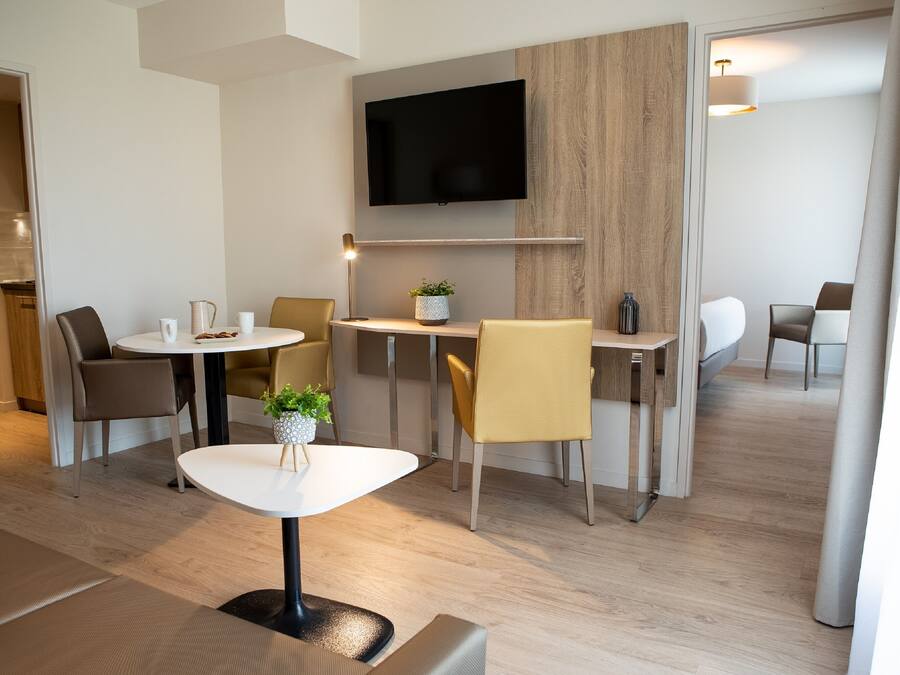 Una habitación de hotel moderna con una televisión de pantalla plana montada en la pared, una mesa redonda con sillas y un sofá.